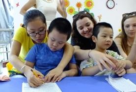 China Childcare volunteers work closely with children from a kindergarten in China, helping them to draw and colour in.