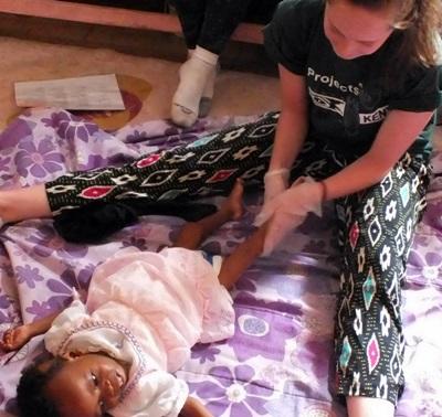 An occupational therapy volunteer works with a little girl in Kenya. An occupational therapy volunteer helps a young girl move her legs in Kenya.
